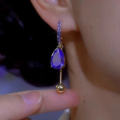 Purple teardrop crystal gold ball dangle hoop earring worn on ear close-up