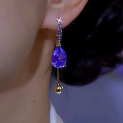 Sparkly purple teardrop crystal gold ball dangle hoop earring on ear side view