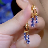 Pair of gold teardrop hoop earrings with graduated purple-blue crystal dangles, held in hand