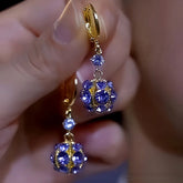 Hand holding gold-tone purple rhinestone ball drop dangle earrings