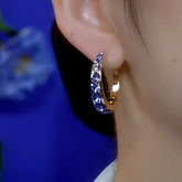 Gold blue crystal huggie hoop earring worn on ear close-up