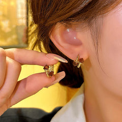 Women's gold twisted mini hoop earrings with brown cube gems, hand holding pair next to ear