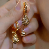 Pair of champagne gold crystal teardrop ball dangle hoop earrings held in hand