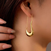 Close-up of polished gold curved teardrop hook earring on woman's ear