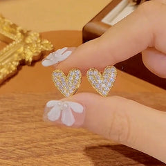 Pair of gold pave rhinestone heart stud earrings held between fingers