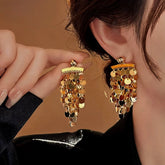 Gold sequin tassel statement drop earrings, one worn on ear, one held in hand