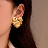 Hammered gold heart stud earring worn on woman's ear, close-up side view