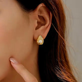 Dainty teardrop gold pearl stud earring worn on woman's ear, close up