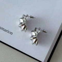 Pair of silver wave sculptural statement hoop earrings on book page