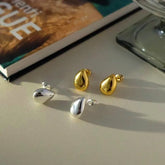 Minimalist gold and silver teardrop stud earring pairs on textured table with magazine