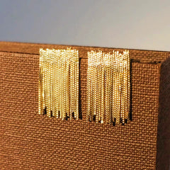 Close-up of gold beaded chain tassel stud earrings on brown textured fabric