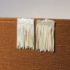 Close-up of silver beaded chain tassel stud earrings on brown woven background