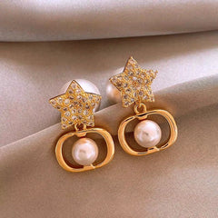 Pair of gold rhinestone star pearl drop earrings on beige satin fabric