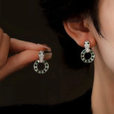 Silver snake head drop earrings with green gem circle, worn on ear and held in hand