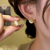Dainty round gold cat's eye stud earring held next to matching worn earring