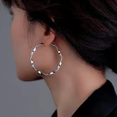 Silver twisted wavy large hoop earring worn on woman's ear, side view