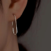 Silver minimalist paperclip-shaped earring worn on ear, close-up