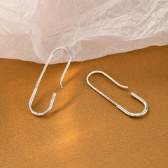 Pair of silver paperclip style earrings flat lay on textured warm surface