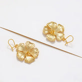 Gold hibiscus flower hook dangle earrings flat lay on white background