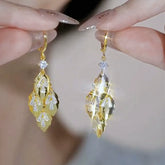 Pair of gold leaf cubic zirconia dangle earrings held by manicured fingers
