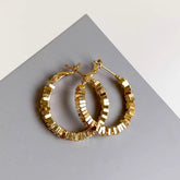Gold cube segmented hoop earrings laid on gray and white surface