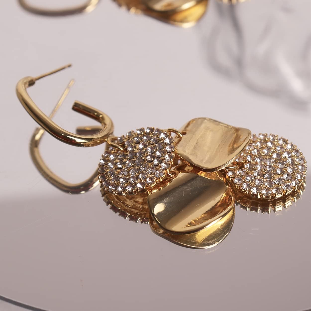 Close-up of gold crystal disc drop earrings on reflective mirror surface