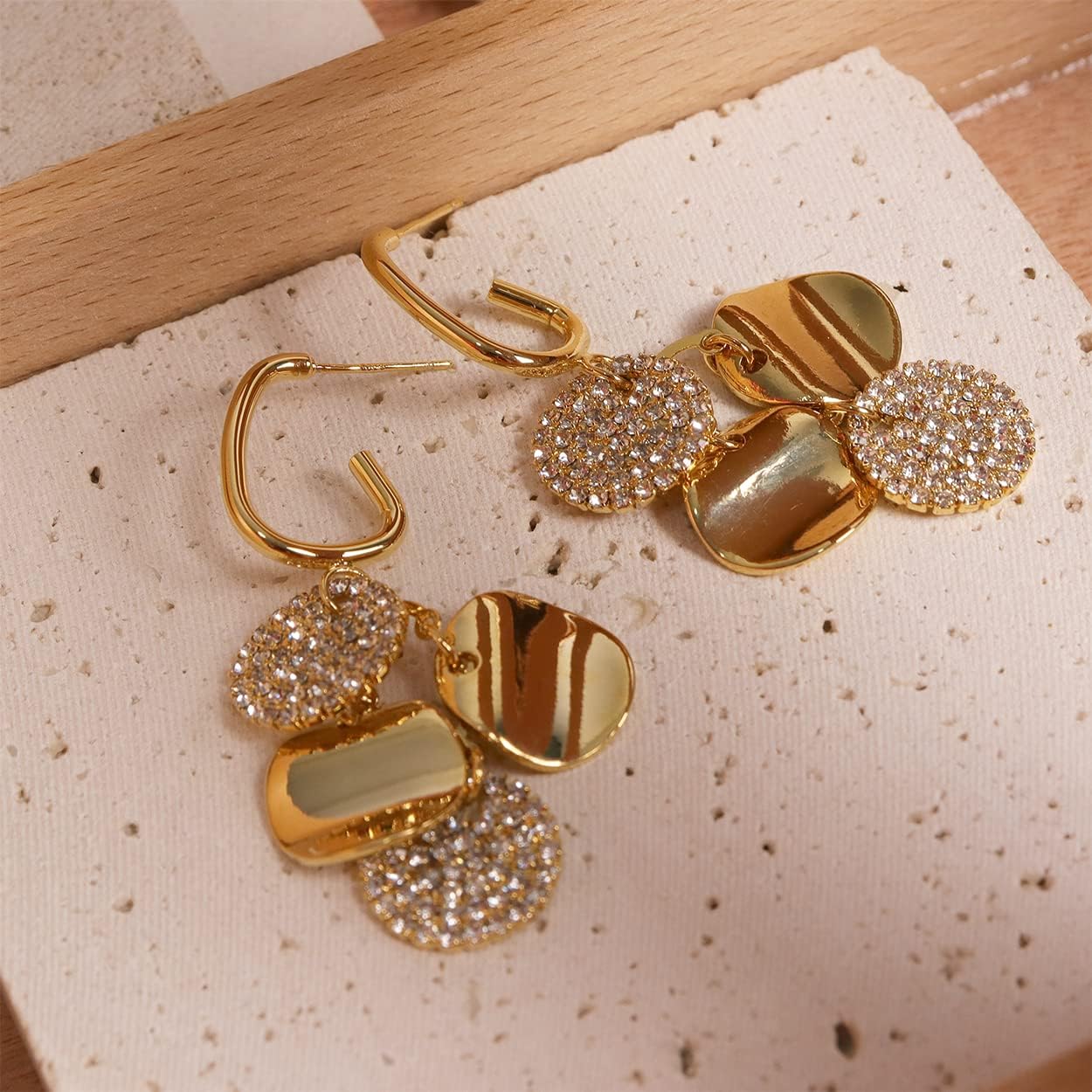 Gold crystal pave disc drop earrings on textured stone display surface