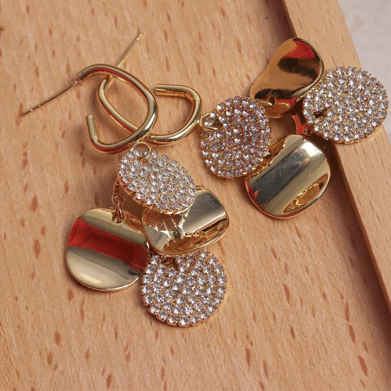 Gold geometric drop earrings with pave crystal discs on wooden surface