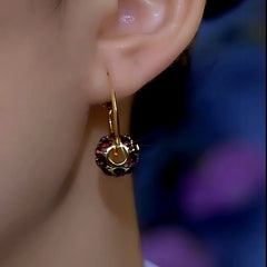 Close-up of purple crystal gold hoop earring worn on a person's earlobe