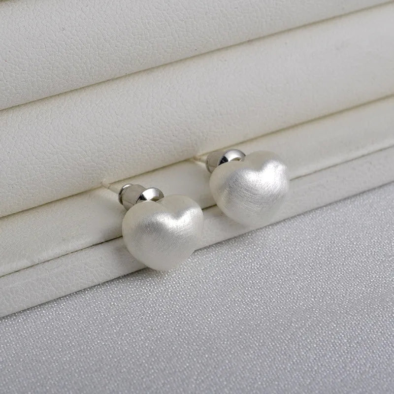 Model showcasing the dangle and style of the 14K Gold-Pated Brushed Heart Stud Earrings