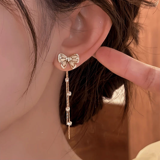 Model showcasing the dangle and style of the 14K Gold-Pated Zircon Bow Tassel Earrings