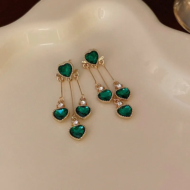 Model showcasing the dangle and style of the 14K Gold-Pated Zircon Green Heart Tassel Earrings