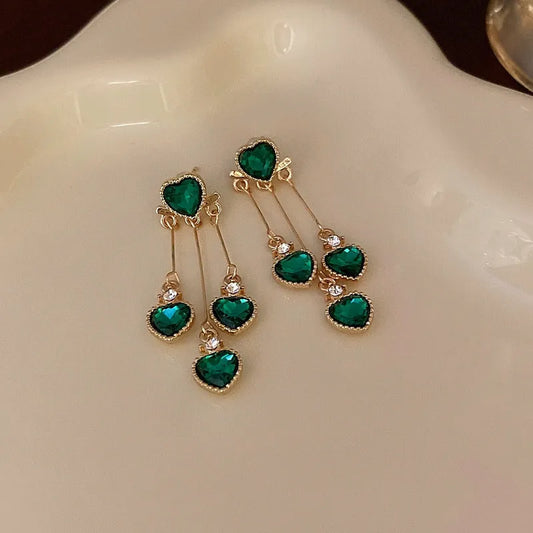 Model showcasing the dangle and style of the 14K Gold-Pated Zircon Green Heart Tassel Earrings