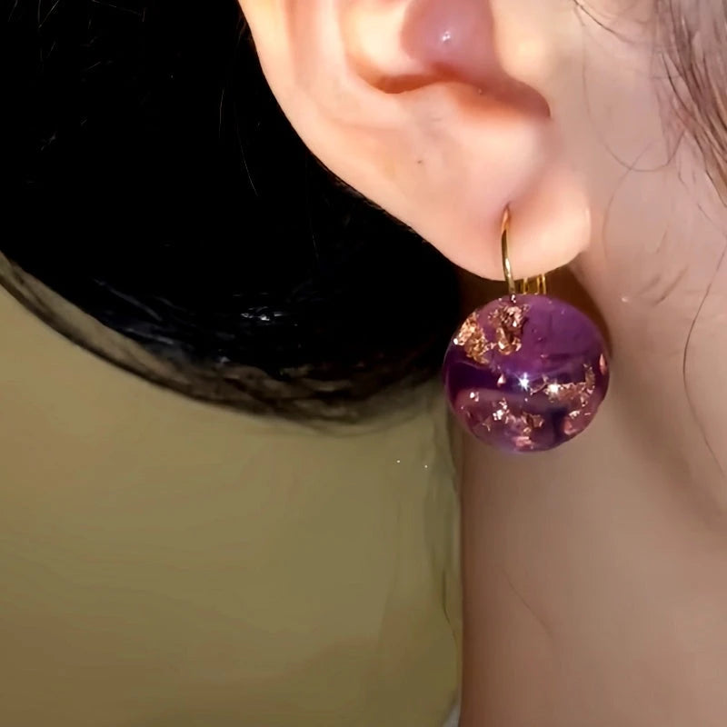 Model showcasing the dangle and style of the 14K Gold-Plated Amber Transparent Ball Earrings