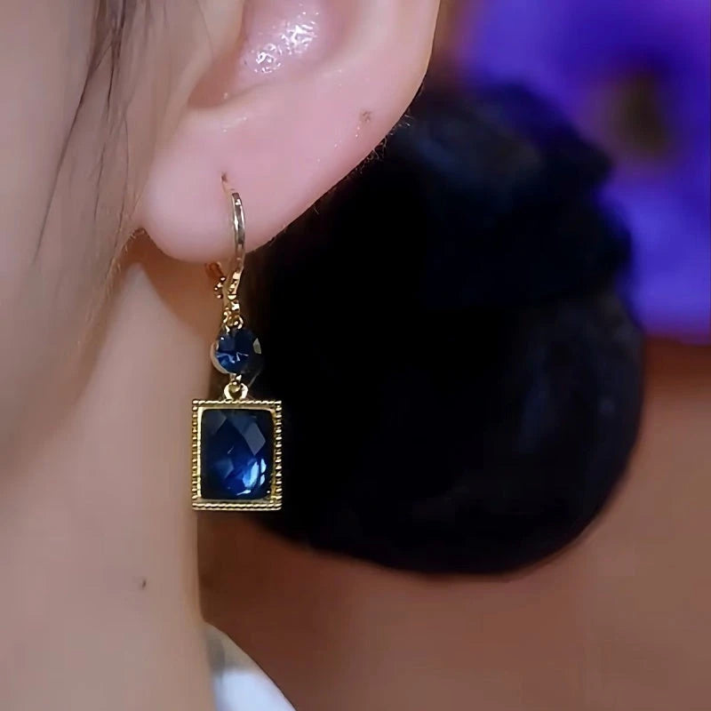 Model showcasing the dangle and style of the 14K Gold-Plated Blue Crystal Earrings