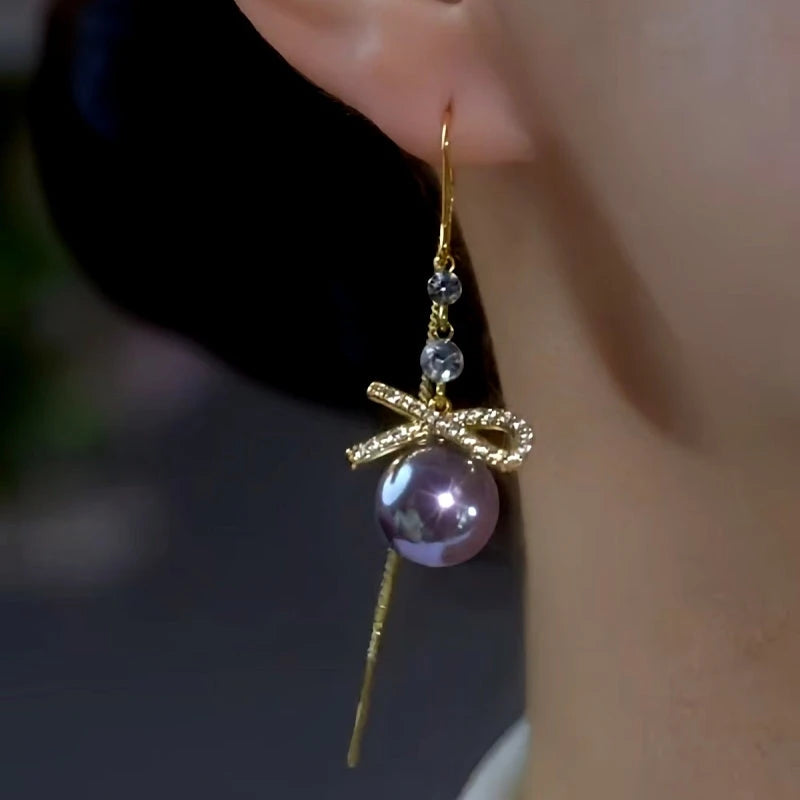 Model showcasing the dangle and style of the 14K Gold-Plated Bowknot Purple Pearl Threader Tassel Earrings