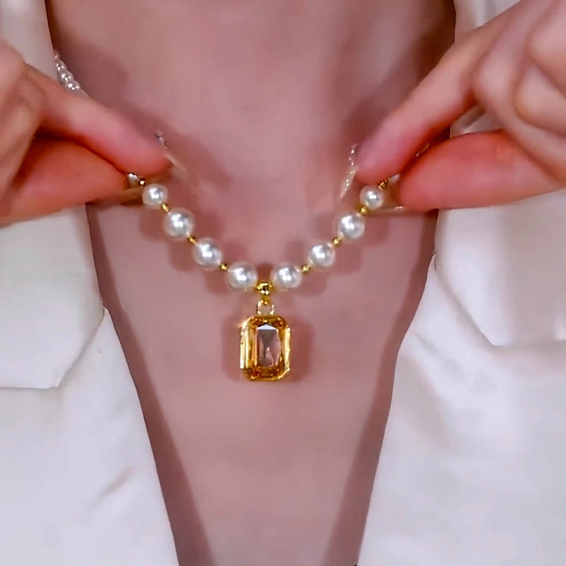 Hands adjusting white pearl necklace, showing back of gold gem pendant