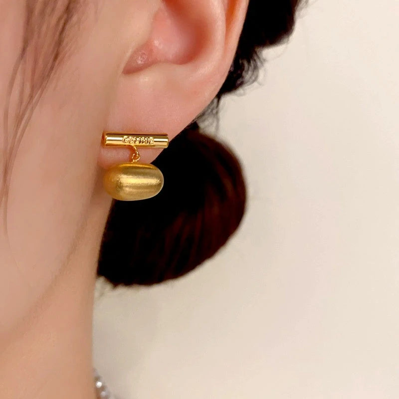 Model showcasing the dangle and style of the 14K Gold-Plated Brushed Bean Earrings