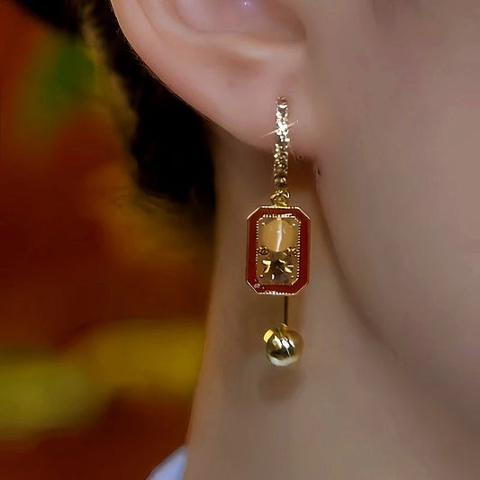 Model showcasing the dangle and style of the 14K Gold-Plated Cat's Eye Stone Brown Diamond Cube Earrings