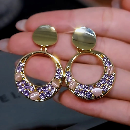 Model showcasing the dangle and style of the 14K Gold-Plated Cat's Eye Stone Purple Diamond Hoop Tassel Earrings