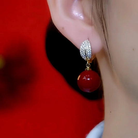 Model showcasing the dangle and style of the 14K Gold-Plated Diamond Leaf Red Bead Earrings
