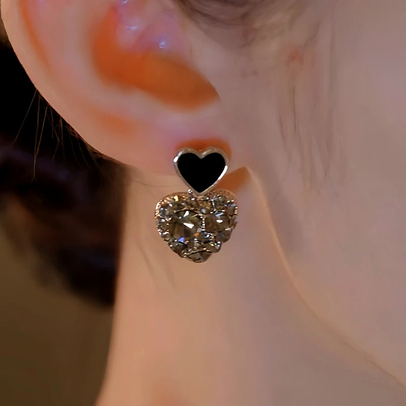 Model showcasing the dangle and style of the 14K Gold-Plated Elegan Black Heart Rhinestone Earrings