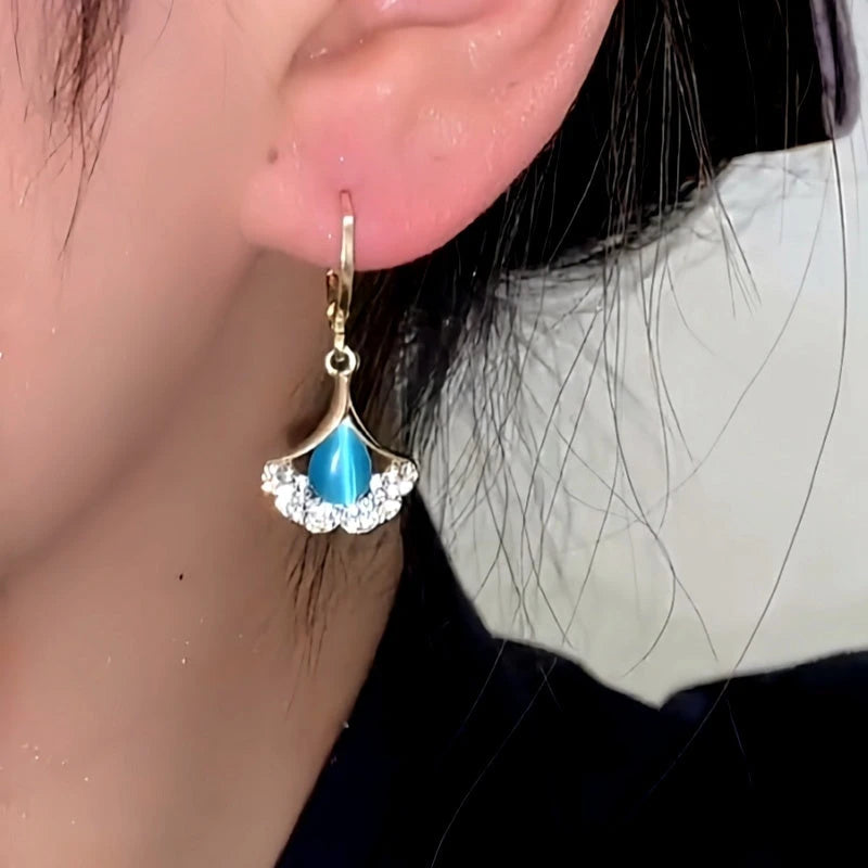 Model showcasing the dangle and style of the 14K Gold-Plated Elegant Blue Cat's Eye Stone Ginkgo Leaf Earrings