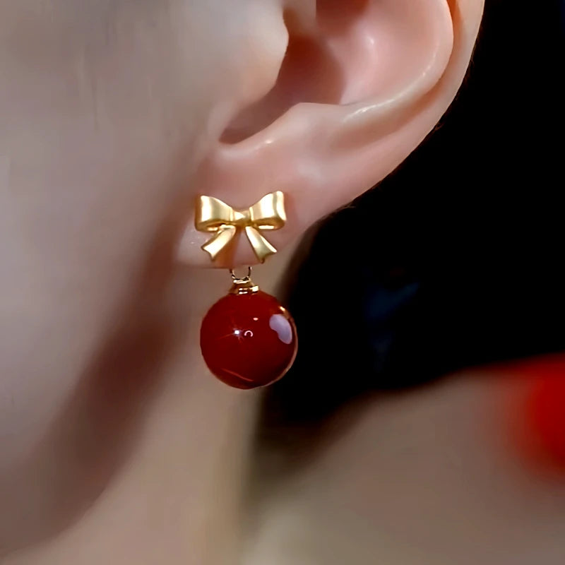 Model showcasing the dangle and style of the 14K Gold-Plated Elegant Bow Red Bead Earrings