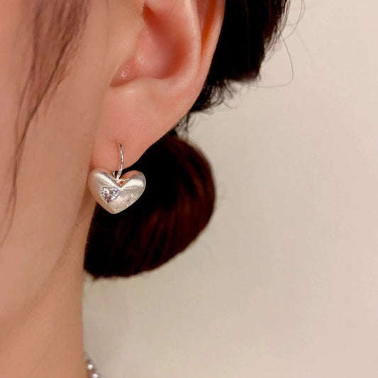 Model showcasing the dangle and style of the 14K Gold-Plated Elegant Brushed Heart Earrings