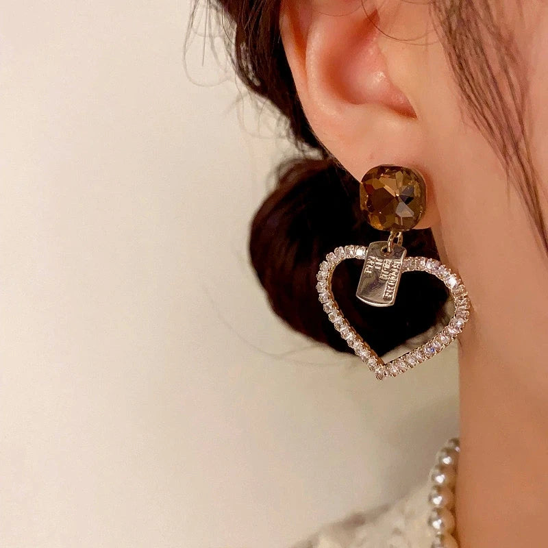 Model showcasing the dangle and style of the 14K Gold-Plated Elegant Diamond Heart Earrings