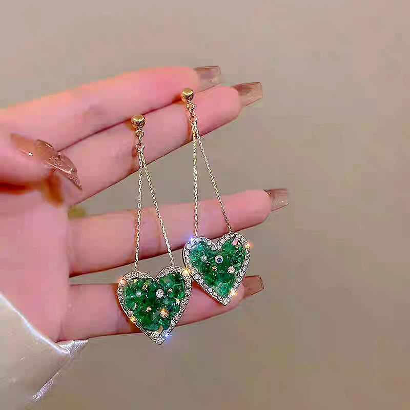 Model showcasing the dangle and style of the 14K Gold-Plated Elegant Green Rhinestone Heart Tassel Earrings