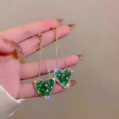 Model showcasing the dangle and style of the 14K Gold-Plated Elegant Green Rhinestone Heart Tassel Earrings