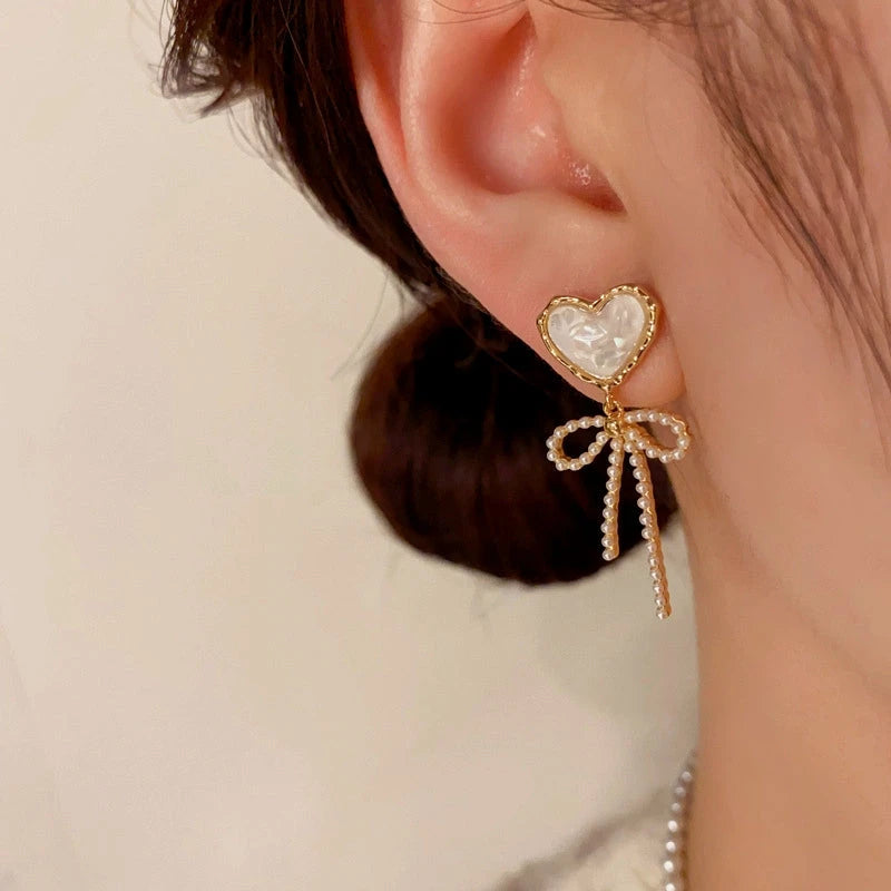 Model showcasing the dangle and style of the 14K Gold-Plated Elegant White Crystal Heart Bow Tassel Earrings