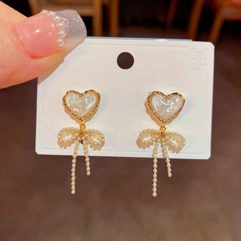 Angled view of the 14K Gold-Plated Elegant White Crystal Heart Bow Tassel Earrings